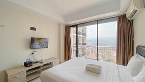 A hotel room with a large bed, a TV mounted on the wall, and a balcony with a view of the city. - Highrise Studio At Apartment Beverly Dago (Bandung)