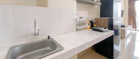 A modern kitchen with white tiles, a stainless steel sink, and a black countertop.
