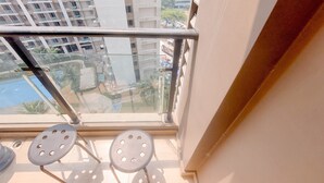 A balcony with a glass railing, two metal chairs, and a view of surrounding buildings and a swimming pool. - Good Place And Strategic Studio At Sky House Bsd Apartment (Pagedangan)