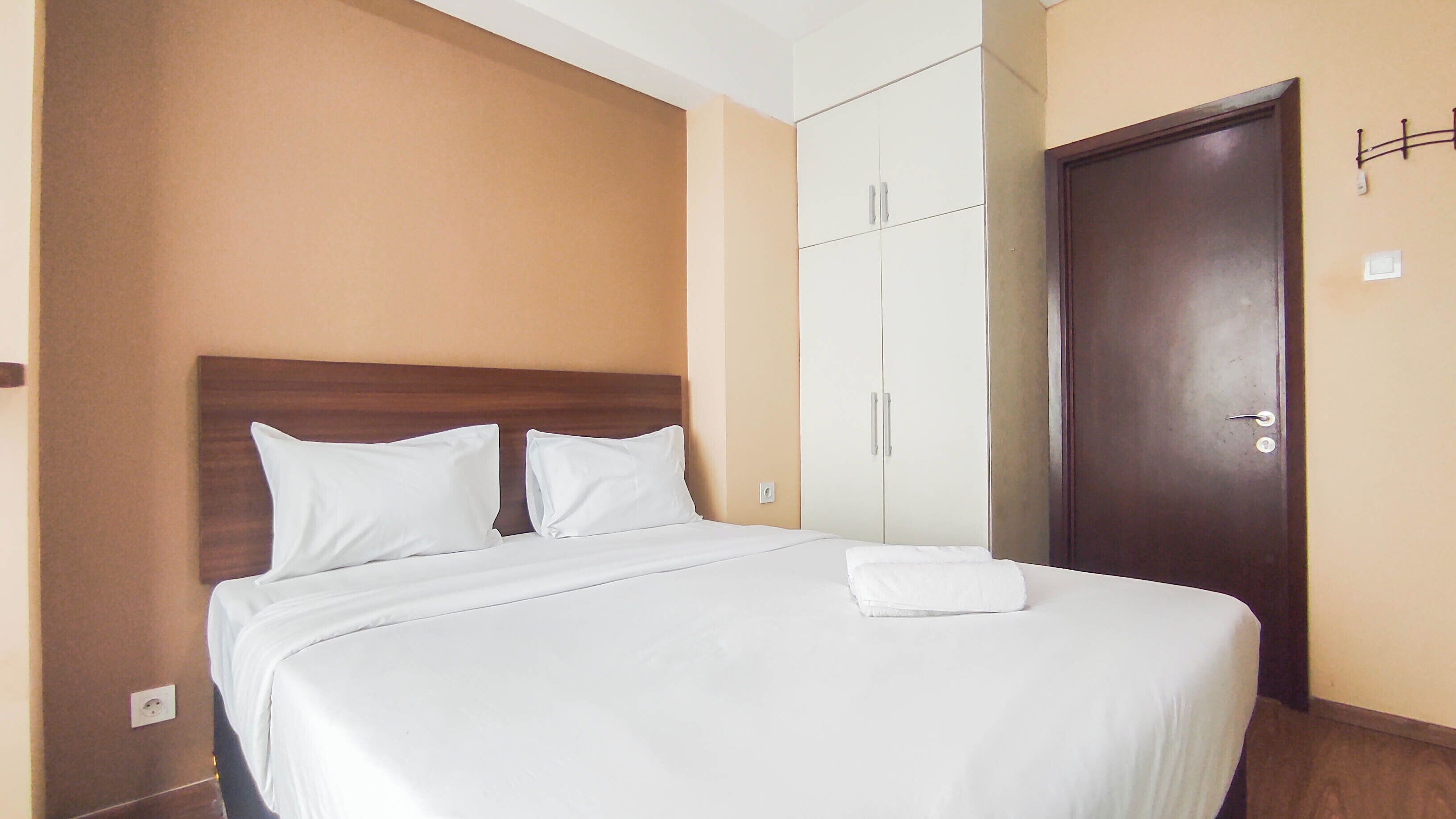 A neatly made bed with white bedding in a room with beige walls and a wooden door.