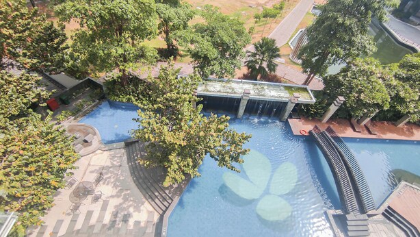 Vista aérea de una piscina con cascada, rodeada de abundante vegetación y un sendero pavimentado.