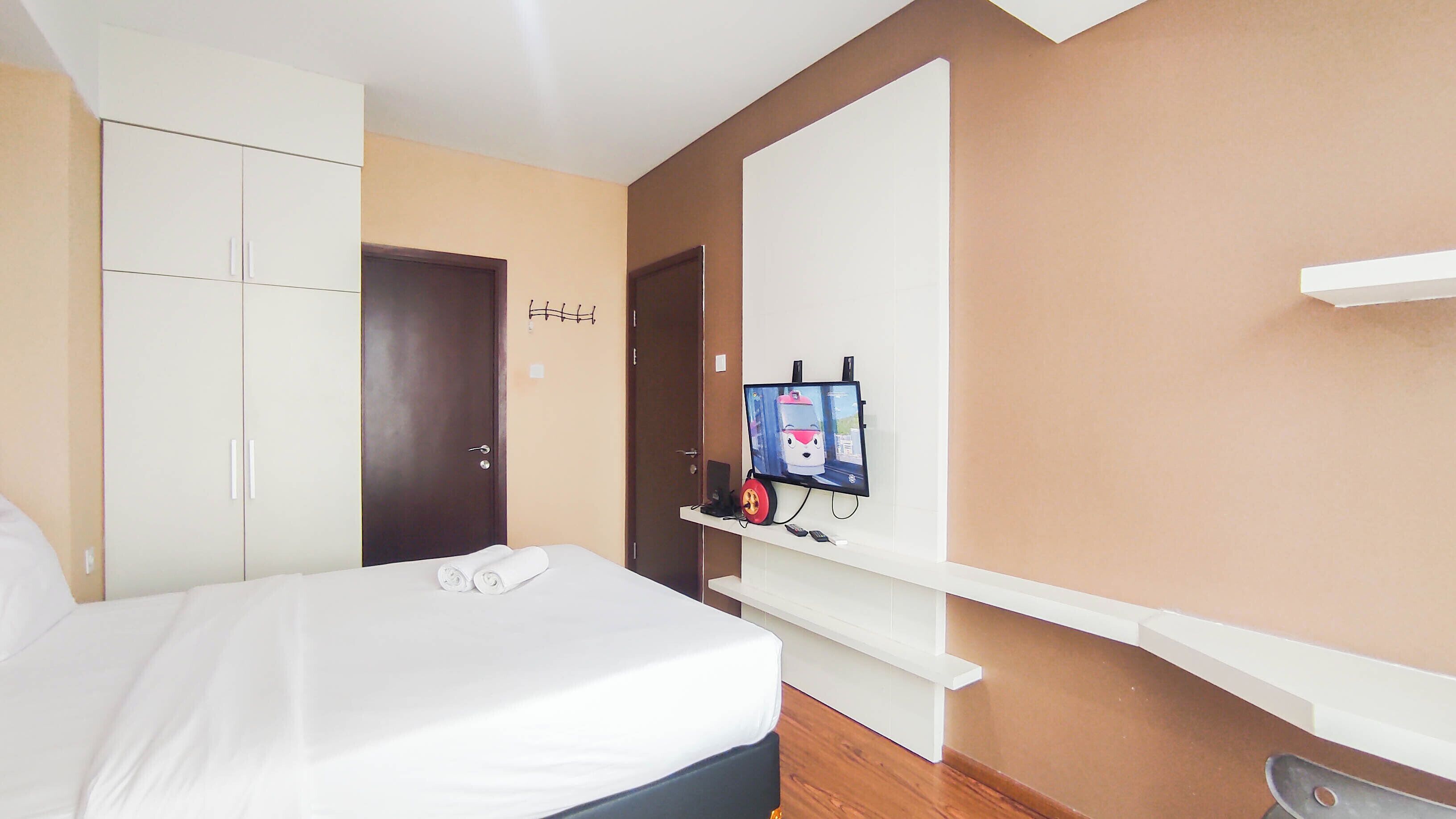 Een hotelkamer met een bed, een kledingkast, een aan de muur bevestigde televisie en een klein plankje met spullen.