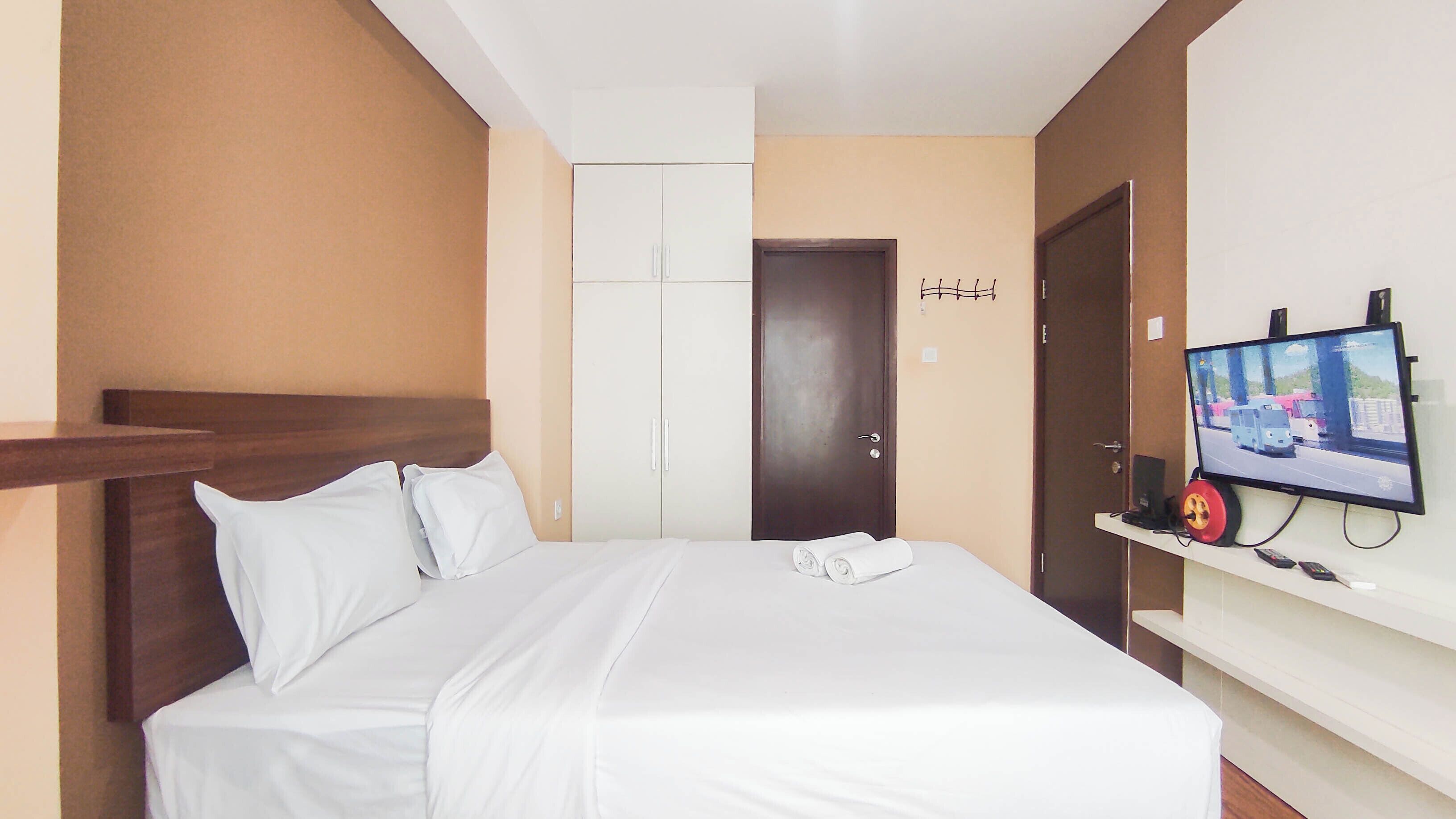 A hotel room with a bed, a TV mounted on the wall, a door, and a coat rack.