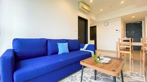 A blue sofa with a small table in front, a wooden chair, a black door, and a clock on the wall.