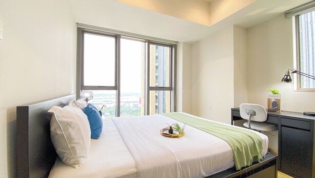 A modern hotel room with a large bed, a desk, a chair, and a window with a city view.