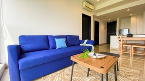 A modern living room with a blue sofa, a wooden coffee table, and a kitchen area in the background.