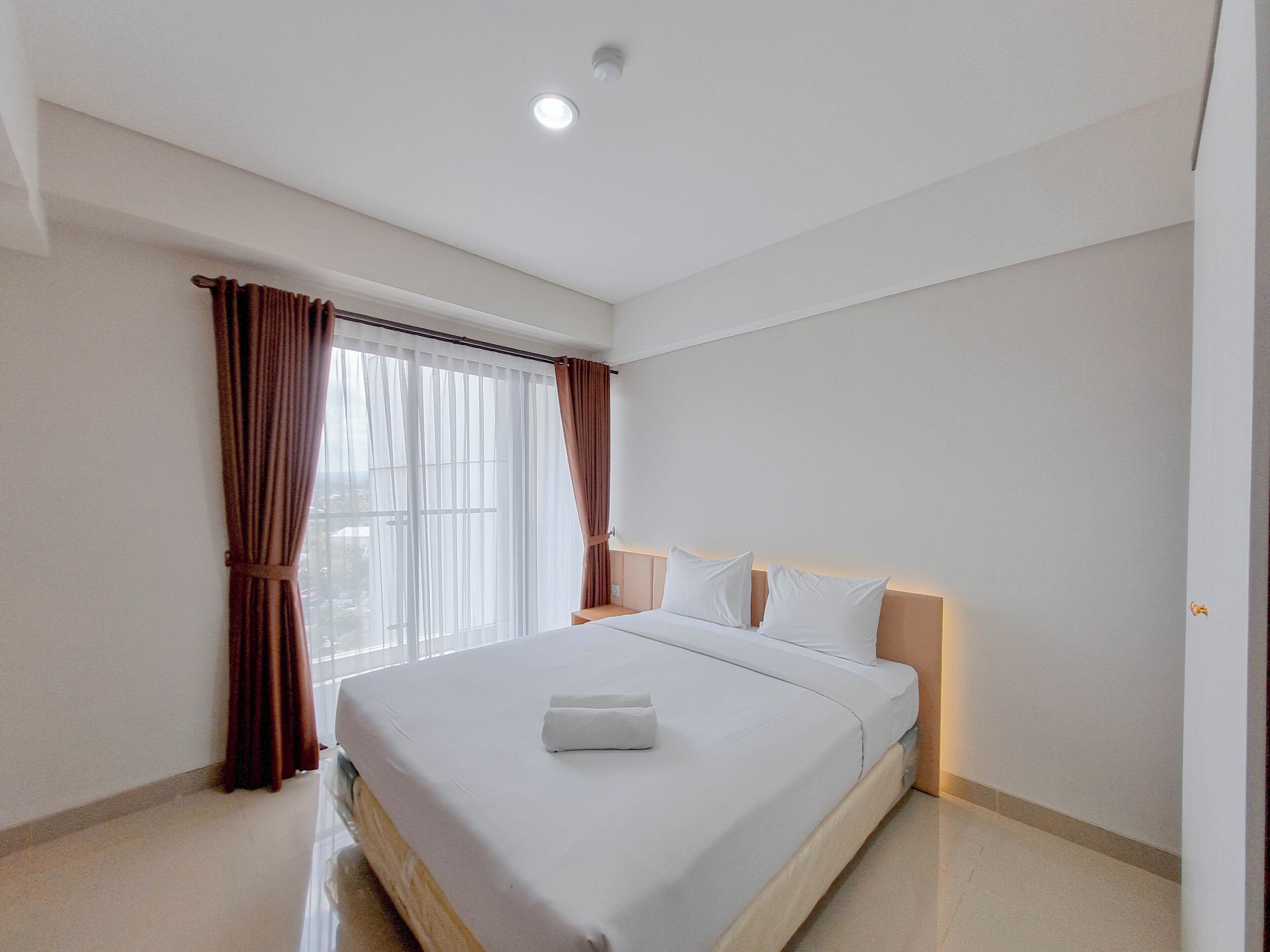 A modern hotel room with a large bed, white linens, and a view through sheer curtains.