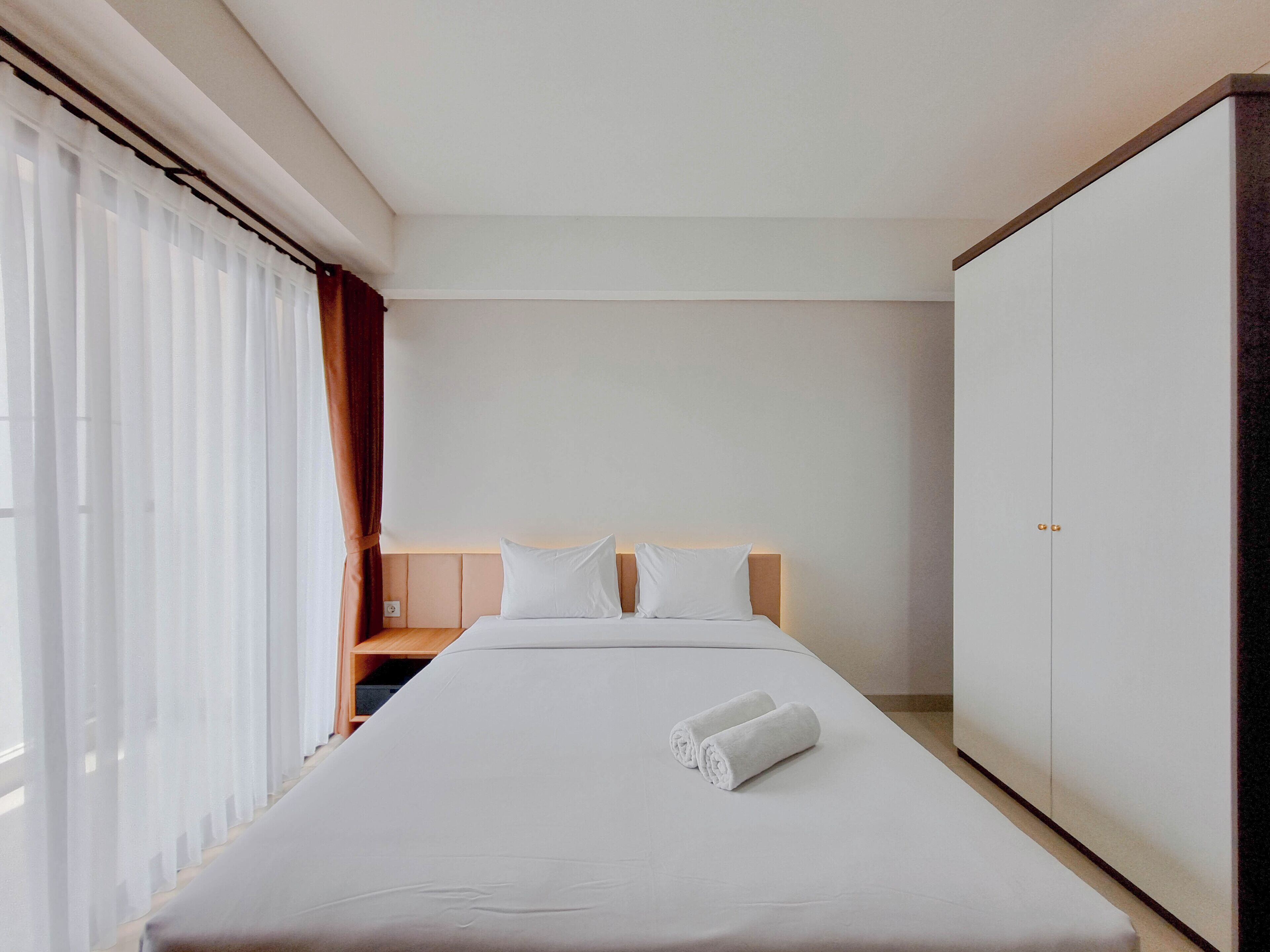 A hotel room with a bed, a wardrobe, and a window with curtains.