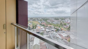 A balcony with a glass railing overlooking a residential area with houses and a dome-shaped building. - Relaxing And Cozy Studio Patraland Amarta Apartment (Ngaglik)