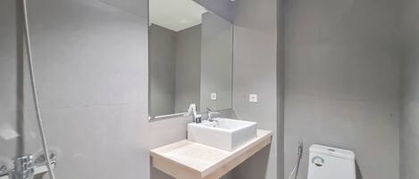 Un baño moderno con lavamanos, espejo, inodoro y ducha.