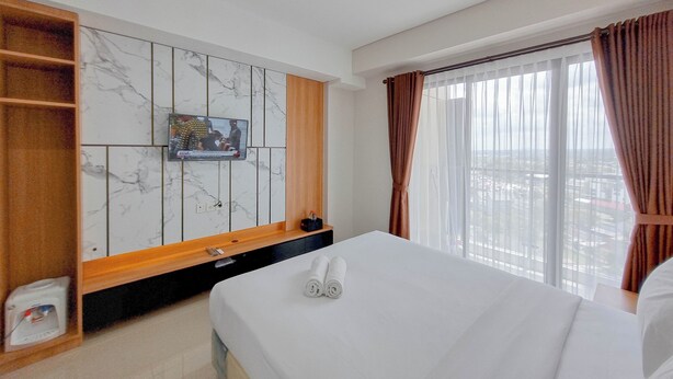 A hotel room with a bed, a TV mounted on the wall, a wooden shelf, and a window with curtains. - Relaxing And Cozy Studio Patraland Amarta Apartment (Ngaglik)