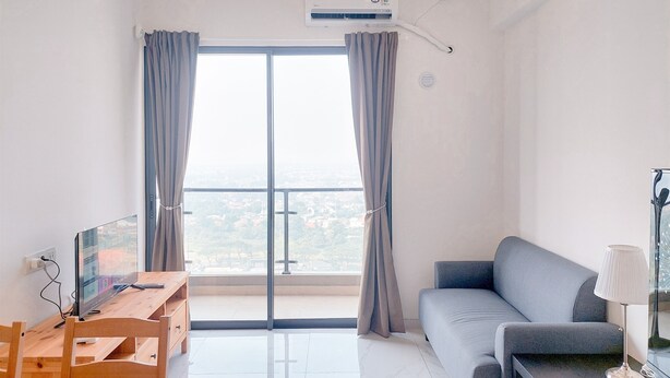 A modern living room with a large window, a sofa, a dining table, and a TV. - Best Place And Homey 2Br Sky House Bsd Apartment Near Aeon (Pagedangan)