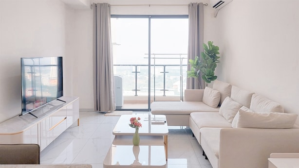 A modern living room with a sofa, coffee table, TV, and a balcony with a plant. - Best Spacious And Homey 3Br Sky House Bsd Apartment (Pagedangan)