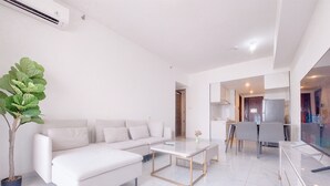 A modern living room with a white sofa, a coffee table, and a potted plant. - Best Spacious And Homey 3Br Sky House Bsd Apartment (Pagedangan)