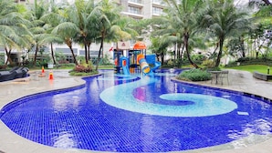 A swimming pool with a blue mosaic design, surrounded by palm trees and a children's play area. - Best Spacious And Homey 3Br Sky House Bsd Apartment (Pagedangan)
