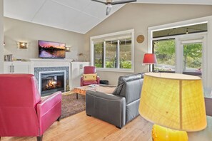 A living room with a fireplace, leather sofas, a TV, and large windows.