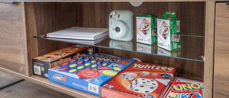 A wooden shelf with various board games, a white camera, and green boxes of InstaFilm film.