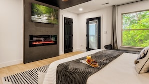 A modern bedroom with a fireplace, a large TV, and a bed with a breakfast tray.