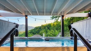 A hot tub with a view of mountains and trees, under a covered area with string lights.