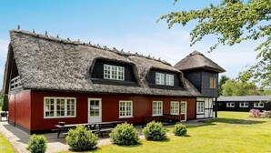 A traditional building with a thatched roof and red walls, featuring multiple windows and a well-maintained lawn. - Luxury Retreat With Amenities - By Traum Ferienwohnungen (Kjellerup)
