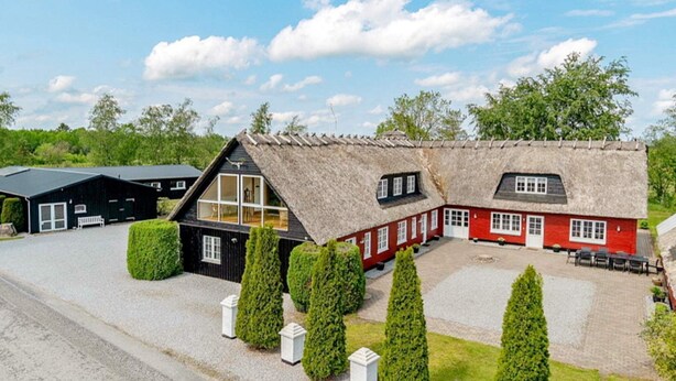 A traditional building with a thatched roof, a red and black exterior, and a gravel driveway. - Luxury Retreat With Amenities - By Traum Ferienwohnungen (Kjellerup)
