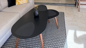 A modern hotel room with a sofa, a small table, a bed, and a large mirror reflecting the room.