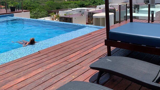 A rooftop pool with a clear view of the ocean, surrounded by greenery and modern buildings.