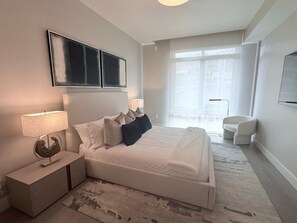 Un dormitorio moderno con una cama grande, mesitas de noche, una lámpara y vistas al exterior.
