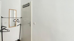 Une pièce avec une porte, un porte-manteau avec des cintres et un miroir.