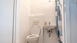 Een kleine, schone badkamer met toilet, wastafel en douchegordijn.