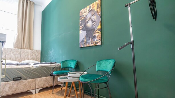 Een kamer met een bed, twee stoelen, een tafel, een schilderij en een microfoonstandaard.