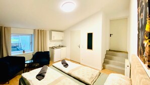 Ett hotellrum med två sängar, ett litet pentry, ett fönster med gardiner, ett skrivbord och en trappa.