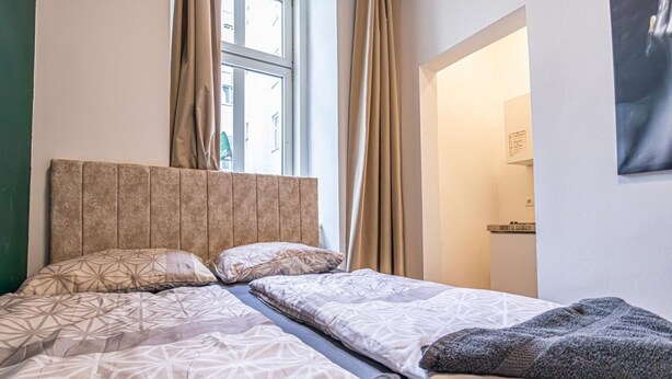 Une pièce avec un lit, une fenêtre avec des rideaux et une porte qui donne sur une autre pièce.