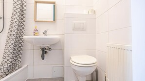 Une salle de bain avec un lavabo blanc, des toilettes et un rideau de douche orné d’un motif en forme d’écailles.