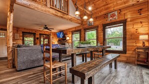 L’intérieur d’un chalet rustique est aménagé avec une table à manger en bois, des bancs, un canapé et un téléviseur.