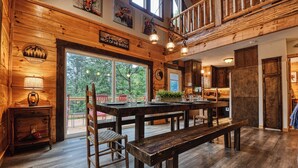 Un intérieur rustique en bois, avec une grande table à manger, des bancs et une vue sur l’extérieur.