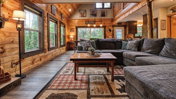 L’intérieur de ce chalet chaleureux est doté d’un grand canapé, d’une table basse en bois et d’une cheminée. De grandes fenêtres laissent entrer la lumière naturelle et offrent une vue sur la forêt.
