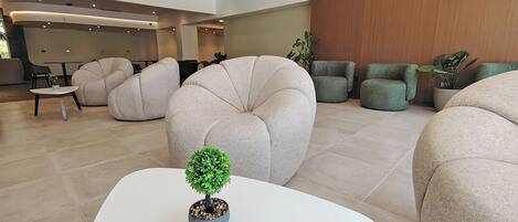 A modern lobby with round seating, a small table with a potted plant, and a reception area in the background.