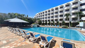 Zona de piscina hotelera con sillones de descanso y un edificio al fondo.