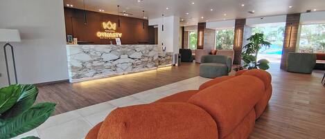 Zona de recepción de hotel con mostrador de mármol, asientos cómodos y vistas al exterior.