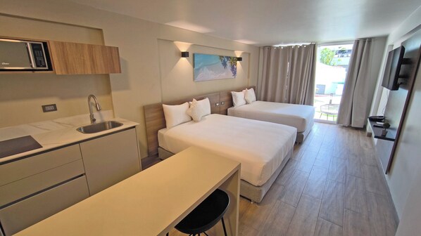 A hotel room with a kitchenette, two beds, a painting, and a TV.