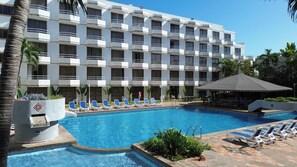 Un hotel con piscina, sillones de descanso y una zona cubierta.