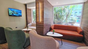 A modern interior with a sofa, chairs, a small table with a plant, and a television on the wall.