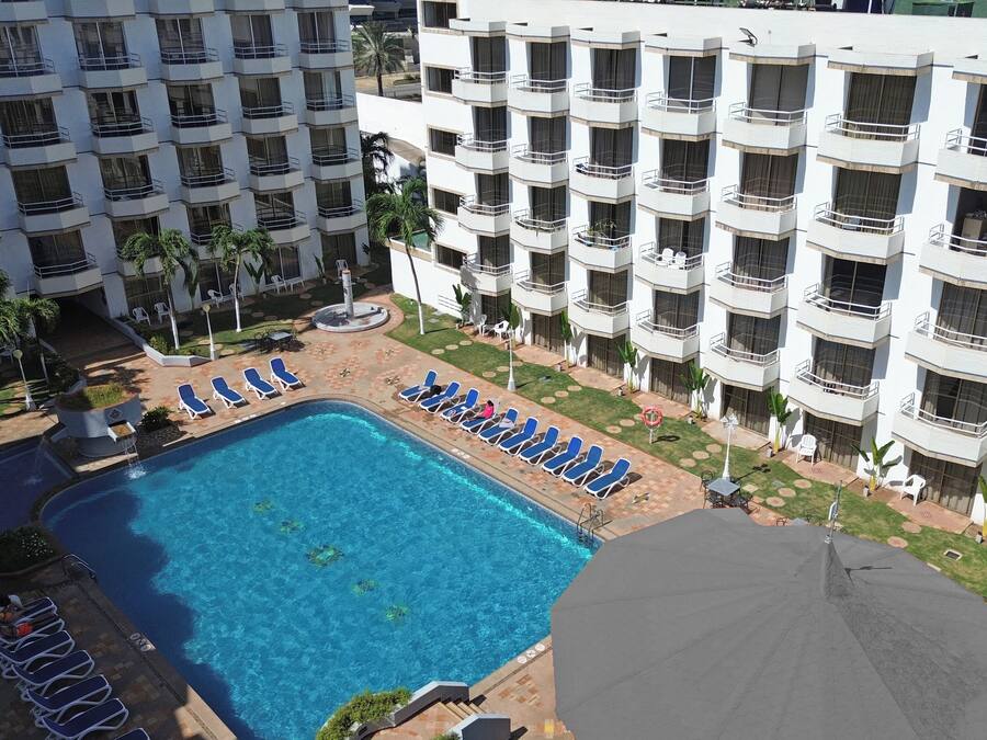 A hotel with a swimming pool surrounded by lounge chairs and a garden area.