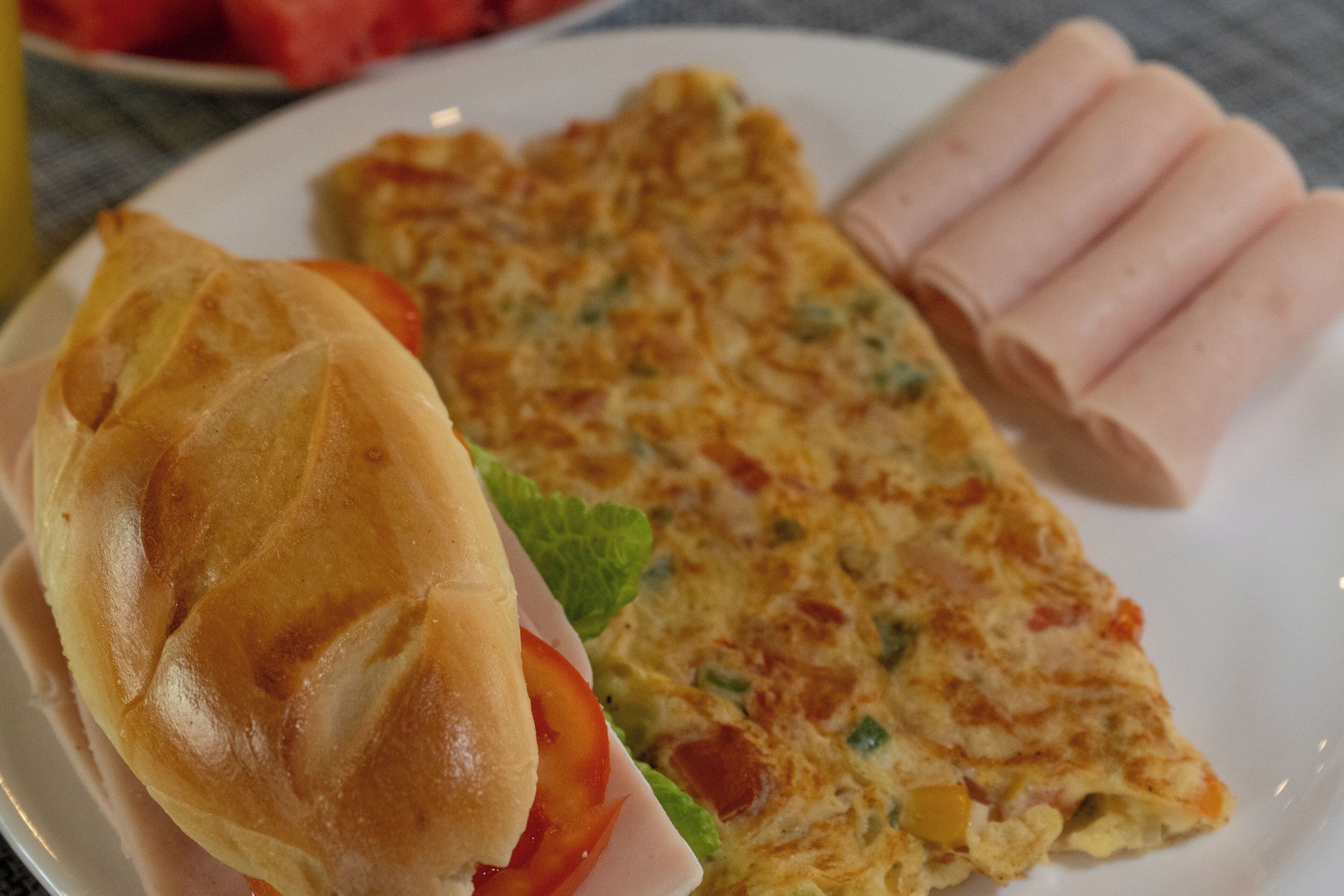 A plate with a sandwich, a slice of omelette, and some meat rolls.
