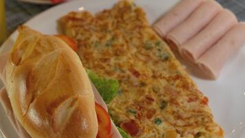 A plate with a sandwich, a slice of omelette, and some meat rolls.