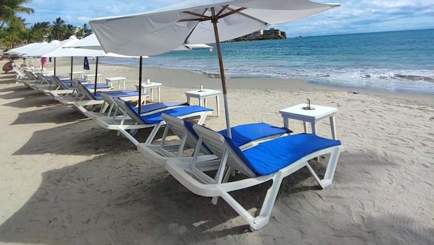 Una playa con sillas de playa blancas y sombrillas, un cielo azul despejado y un mar tranquilo.