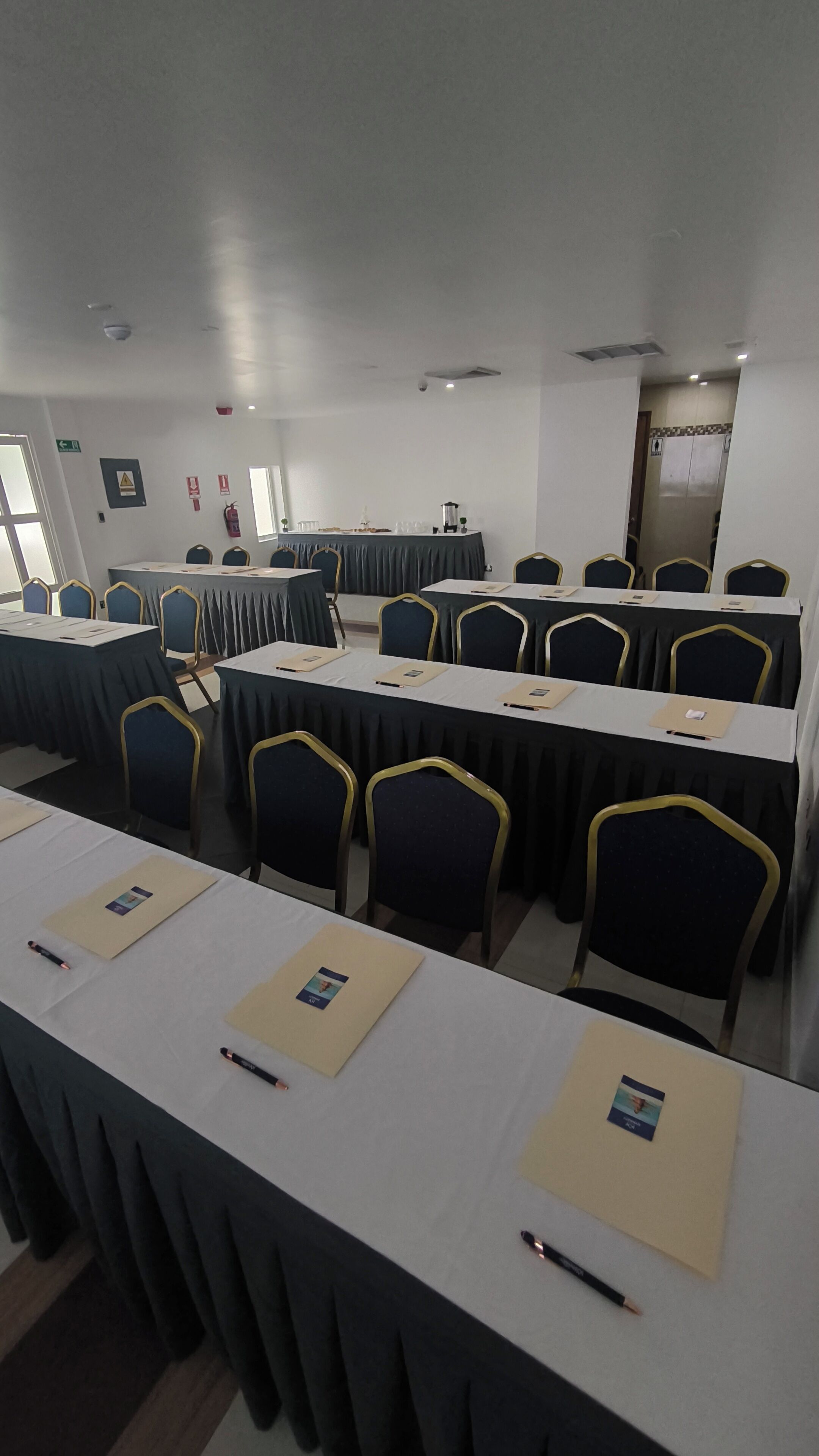 A conference room with long tables and chairs, equipped with nameplates and pens.