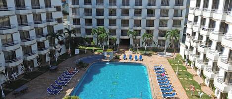 A hotel with a swimming pool surrounded by lounge chairs and palm trees.