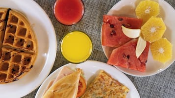 A breakfast plate with waffles, a glass of red juice, a glass of orange juice, watermelon slices, and a sandwich.